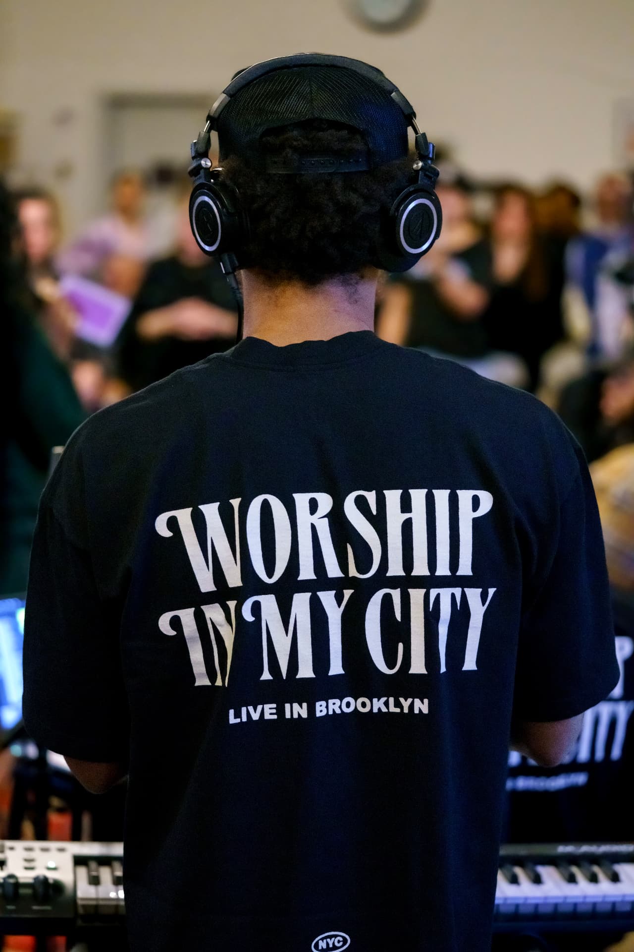 A musician in a Worship In My City — Live in Brooklyn tee, facing the gathering